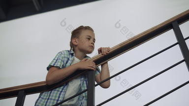 好奇的小学生站楼梯男孩倾斜栏杆检查大厅
